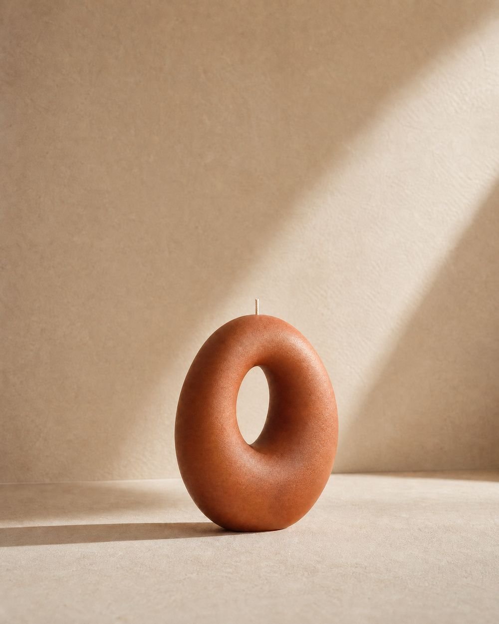 Homey Orbit candle in raking light against a plaster wall